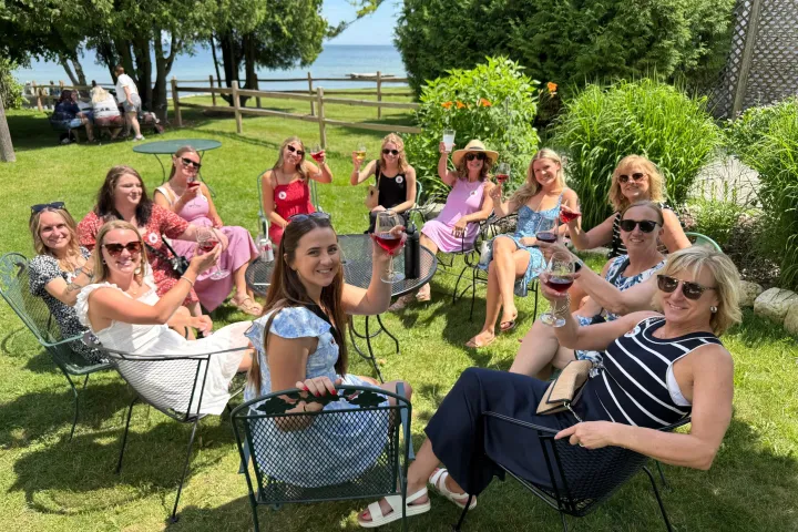 Group of women enjoying drinks in a garden near the water.