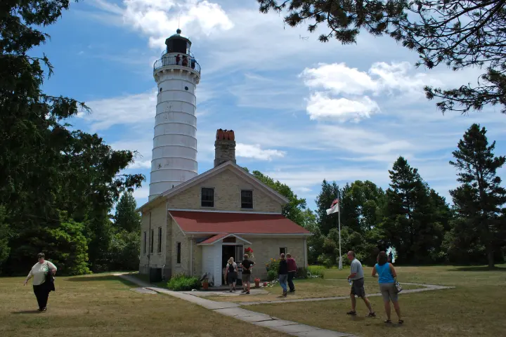 a group of people walking in front of a house with Cana Island Light in the background
