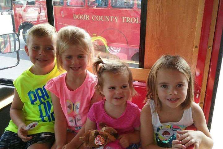 Four children smiling inside a trolley with a 'Door County Trolley' sign visible outside.